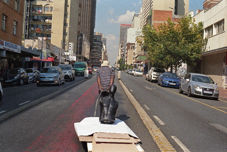 Man walking away from the camera pulling a trolley containg wood and the torso of a mannequin
