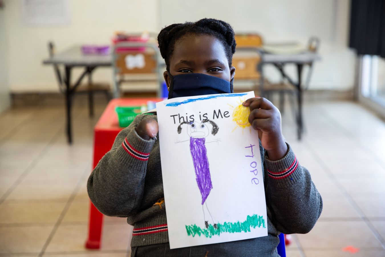 Girl whose right hand is missing holds up a drawing of herself entitled 'This is me' and her name, Hope, is visible on the side of the paper